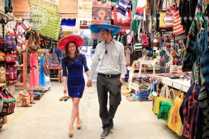Connie Hanks Photography // ClickyChickCreates.com // engagement couple session, Rosarito, Mexico, mercado, market, colorful, turquoise, blue, gray, wood, wheel, rustic, arches, archways, kiss, sombreros