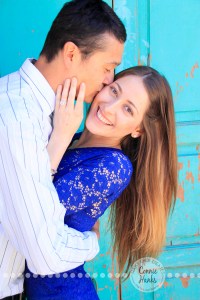 Connie Hanks Photography // ClickyChickCreates.com // engagement couple session, Rosarito, Mexico, mercado, market, colorful, turquoise, blue, gray, wood, wheel, rustic, arches, archways, kiss